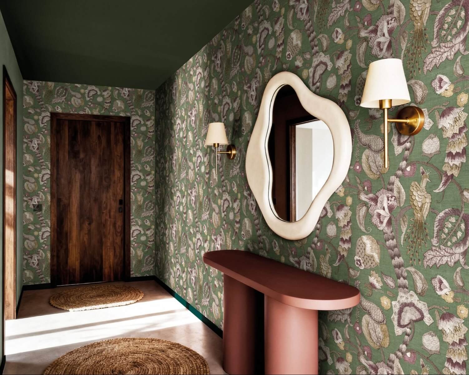 Ambiente corridoio elegante con carta da parati ornamentale JAIPUR verde, specchio organico e consolle moderna.